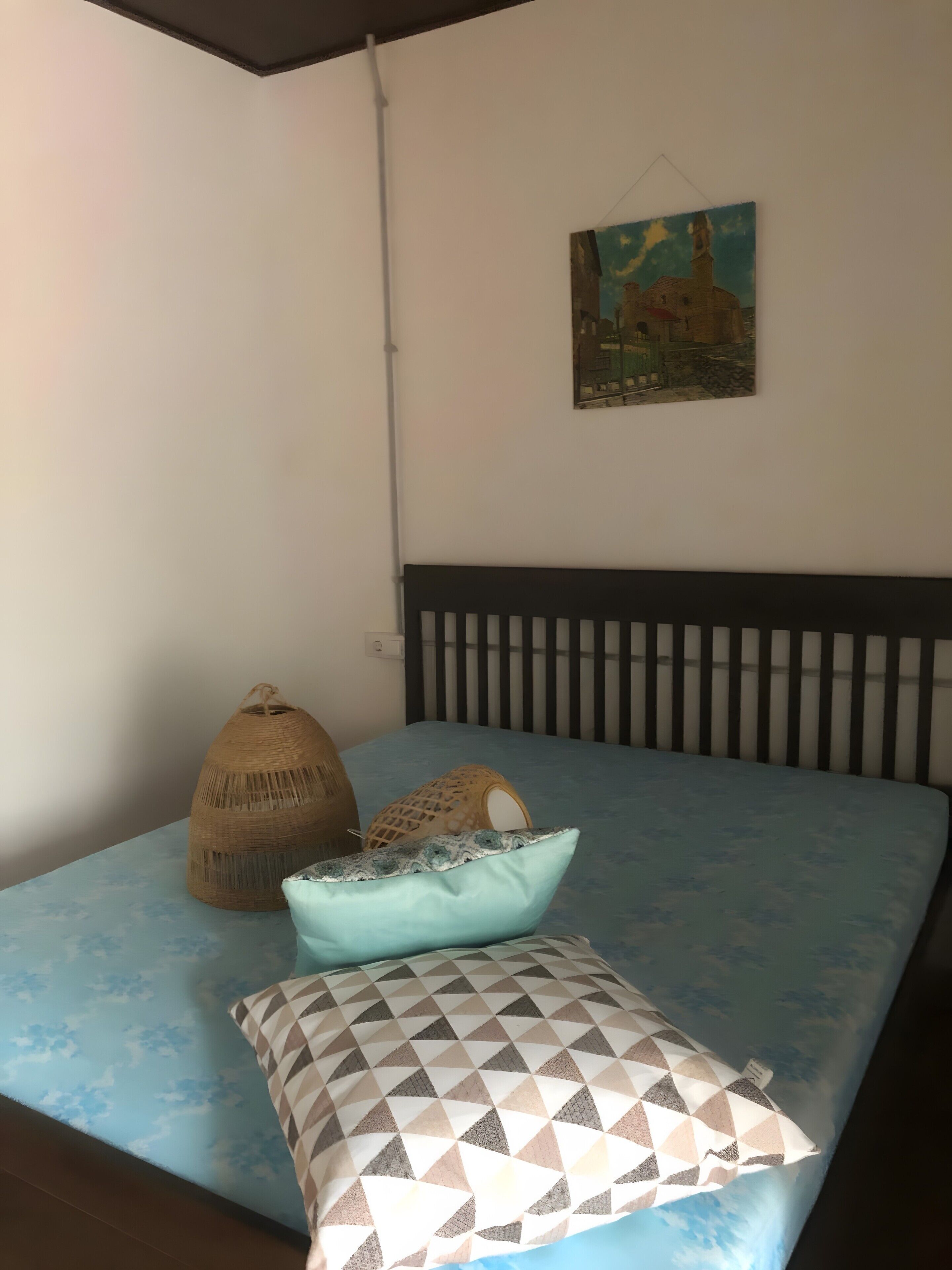 A bed with a blue mattress, a patterned pillow, and a woven basket.