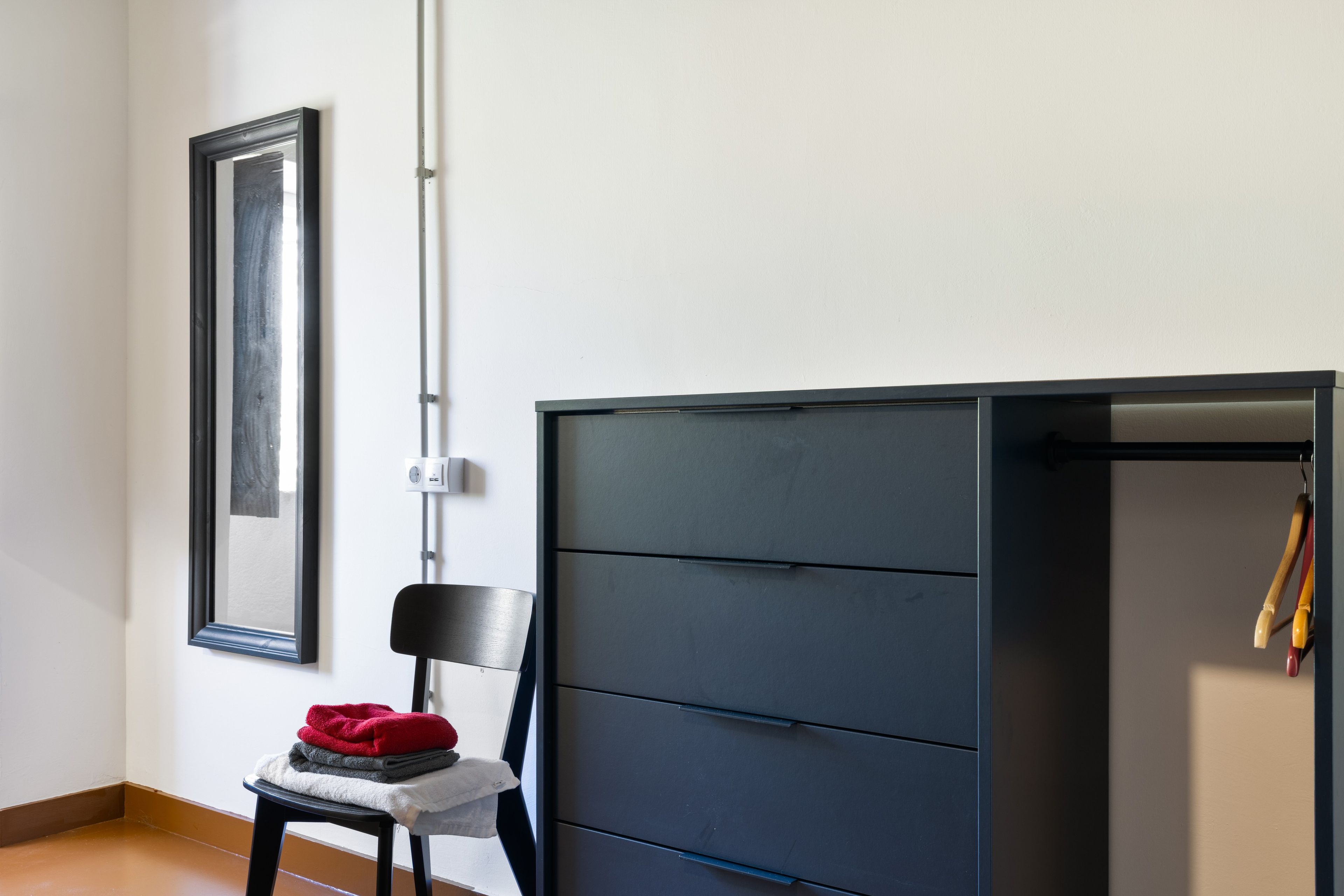 A room with a chair, a large black wardrobe, and a framed picture on the wall.