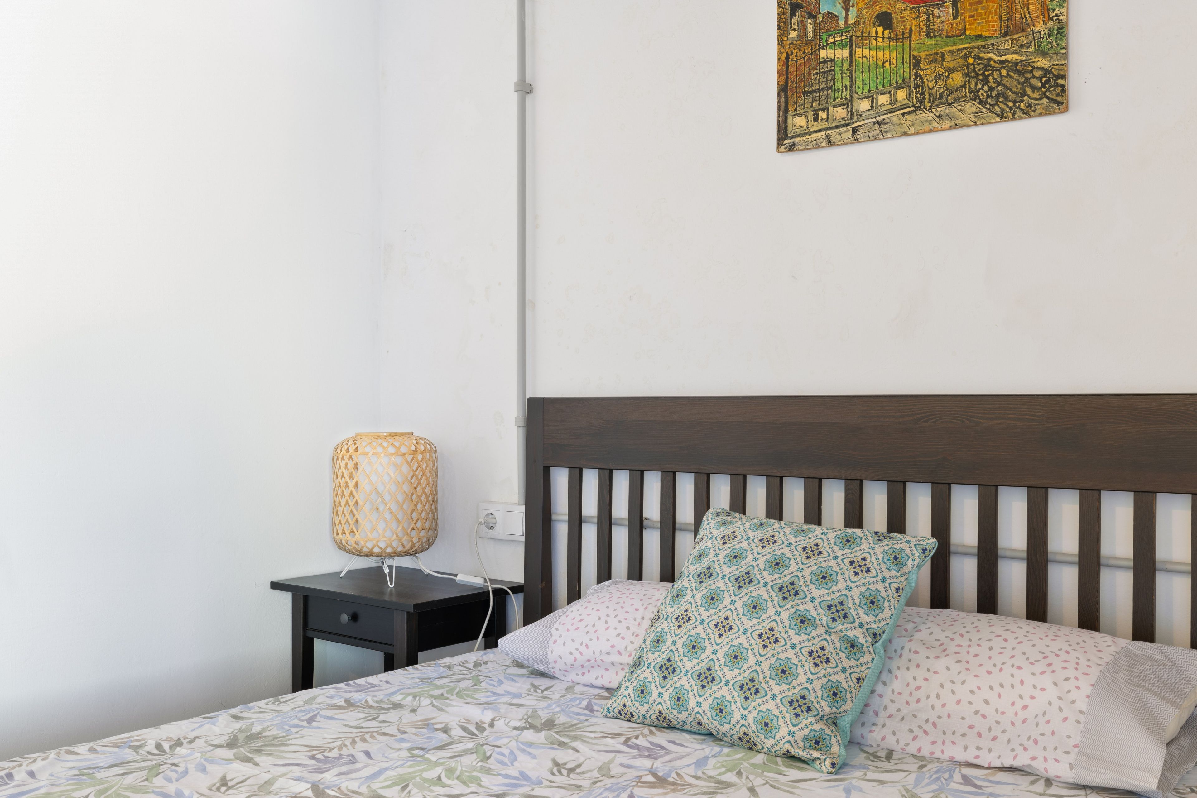Un dormitorio con una cama, una mesita de noche, una lámpara y un cuadro en la pared.