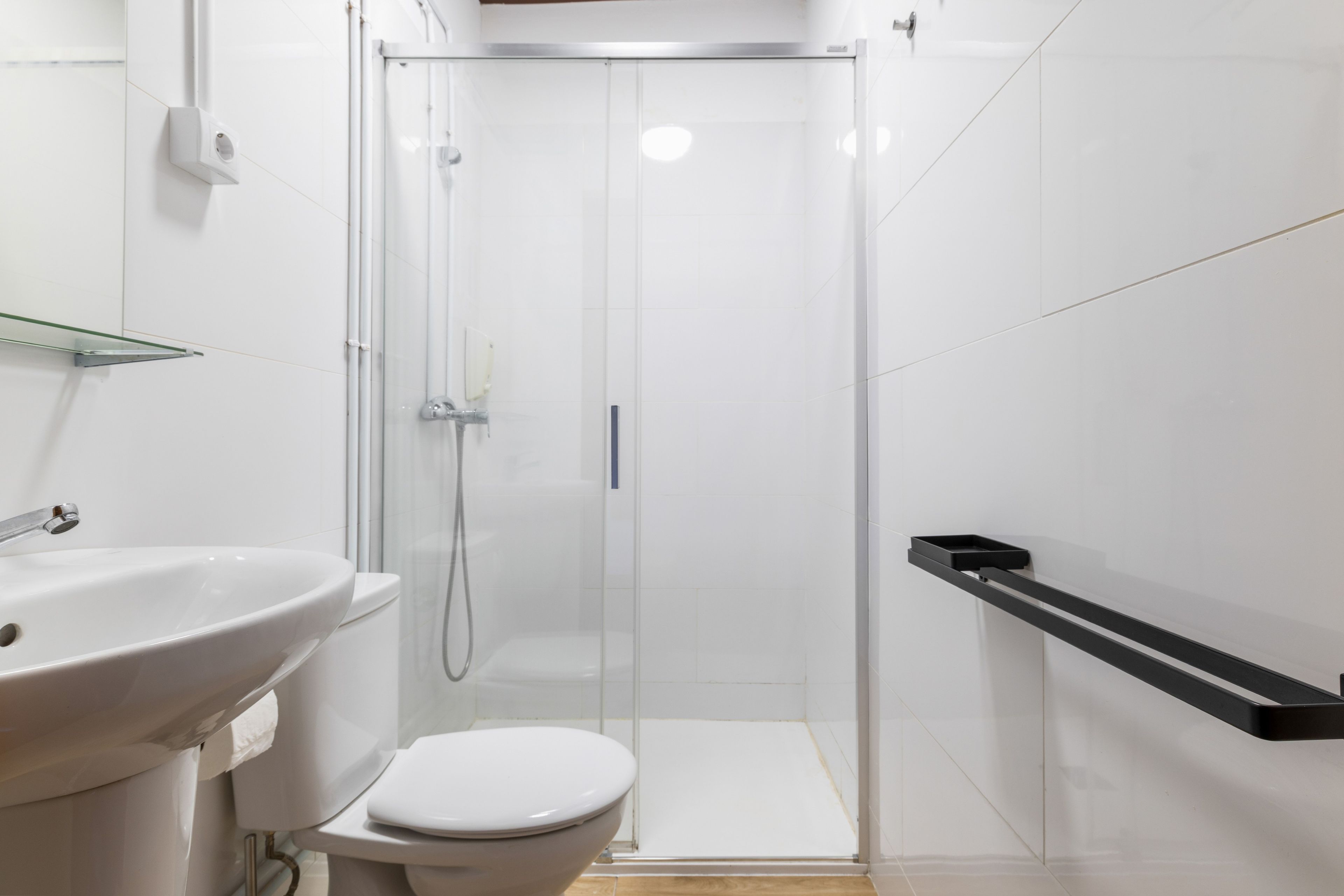 Un baño moderno con cabina de ducha de vidrio, inodoro blanco y lavamanos con estante de vidrio encima.