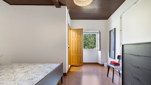 Un dormitori amb un llit, una finestra que ofereix vista a la verdura i una porta que condueix a una altra habitació.