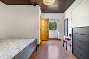 Un dormitorio con cama, ventana con vista a follaje y puerta que conduce a otra habitación.