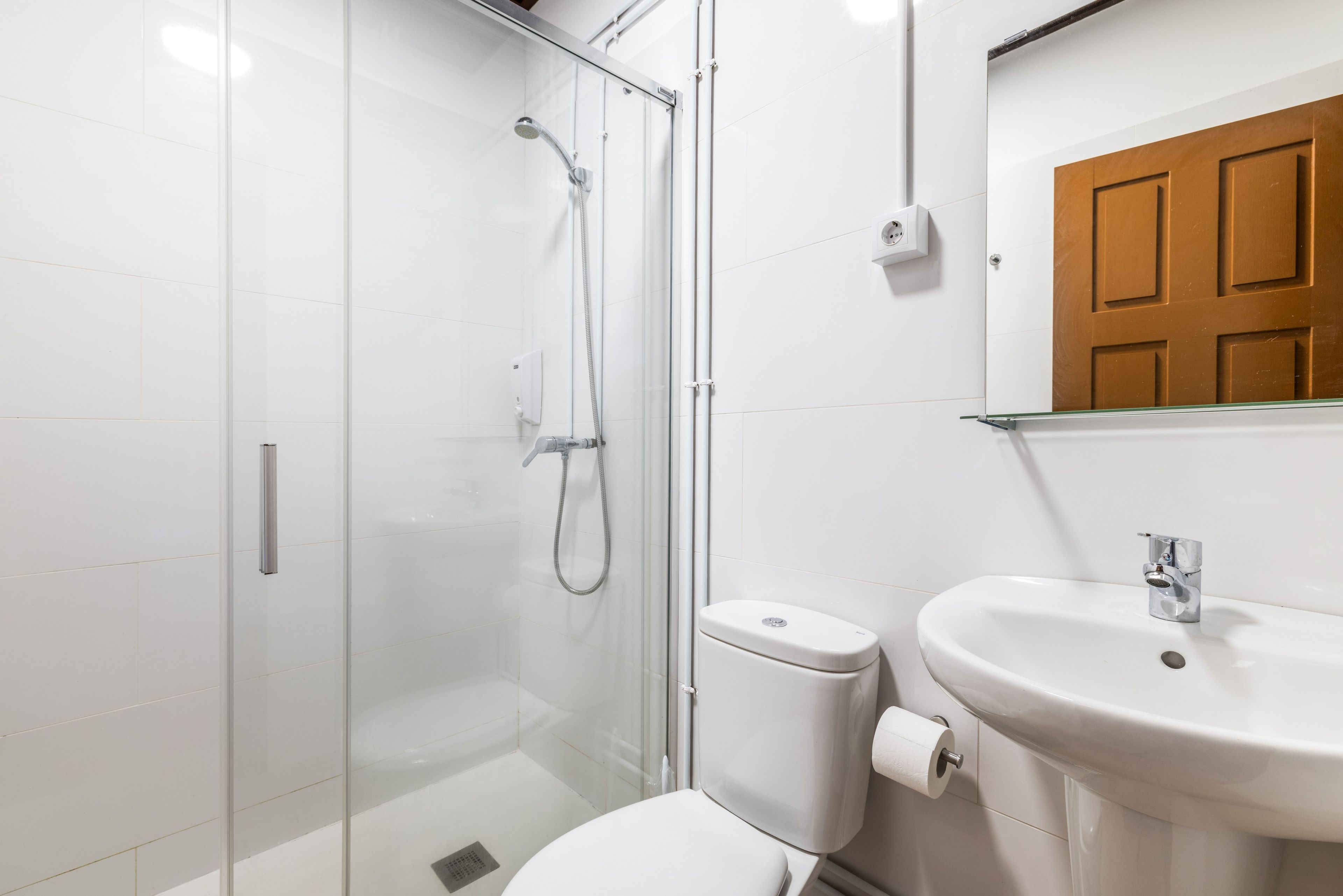 Un baño moderno con ducha envuelta en vidrio, inodoro blanco y lavamanos con espejo superior.