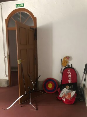 Ein Zimmer mit einer Holztür mit der Aufschrift 'SALIDA', einer Zielscheibe, einem roten Rucksack und einem Stofftier.