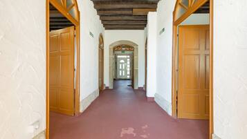 Un pasillo con puertas de madera y suelo rojo, que conduce a un acceso con panel de vidrio.