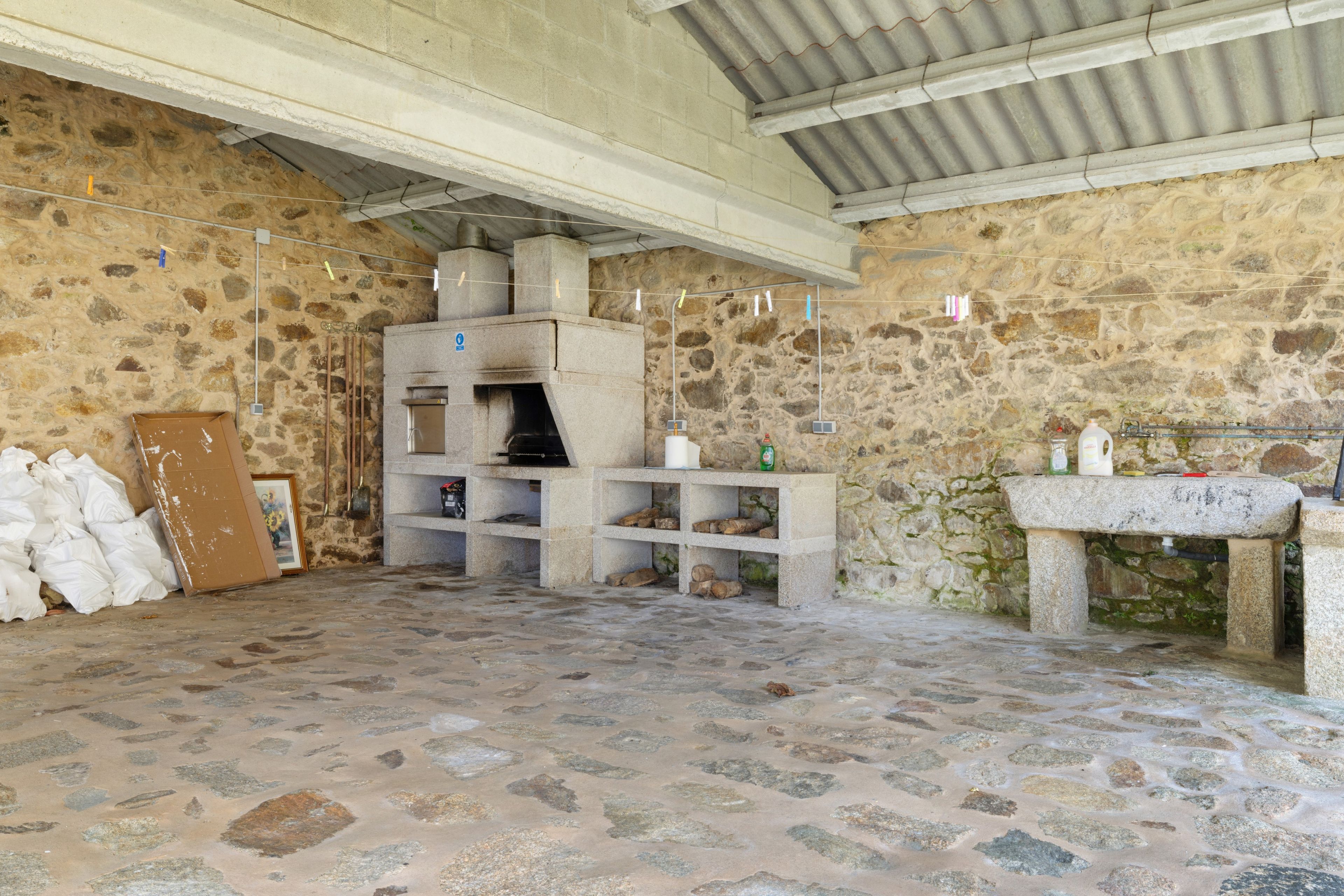 Una habitación de paredes de piedra con un horno de piedra, un banco y una mesa con botellas.