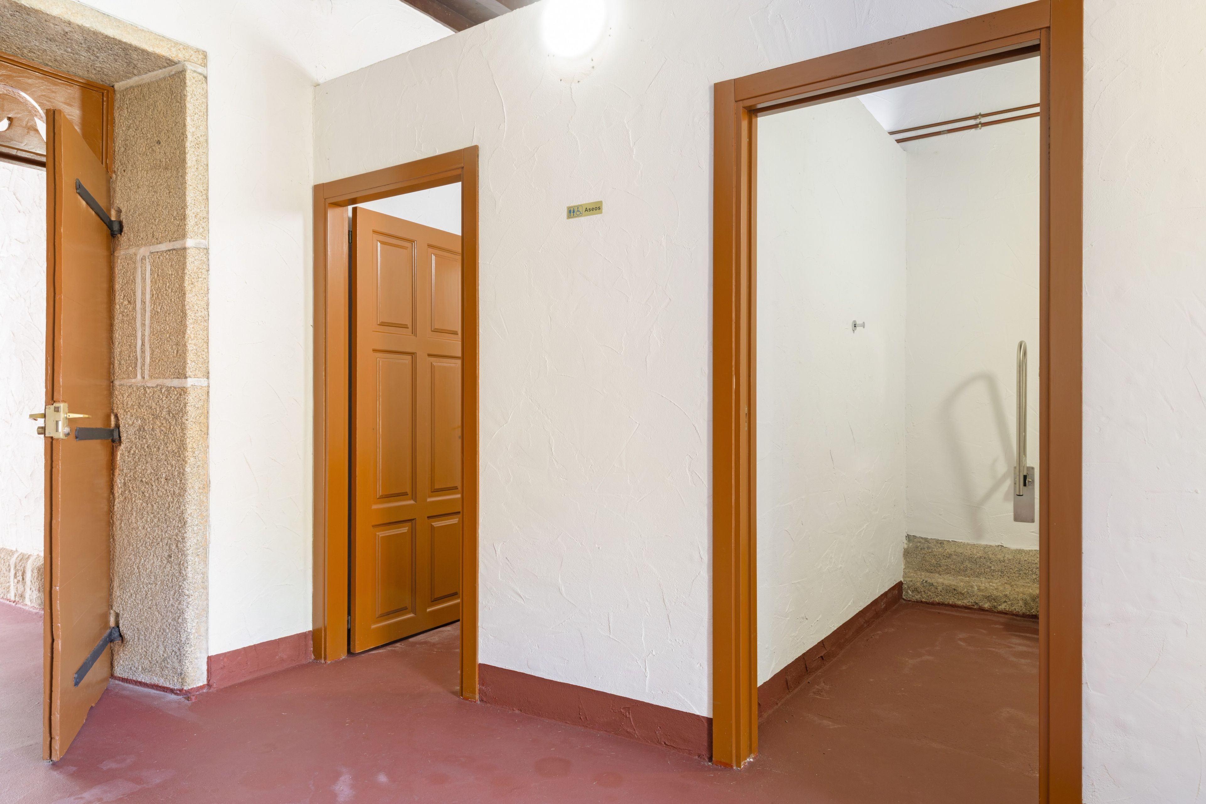 Un pasillo con puerta de madera, pared blanca y suelo rojo.