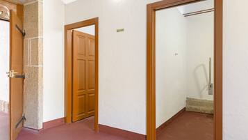 Un pasillo con puerta de madera, pared blanca y suelo rojo.