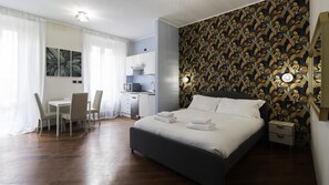 A hotel room with a large bed, a desk with chairs, a kitchenette, and a patterned wall. - Italianway Easy - Venezia 33 - A (Milan)