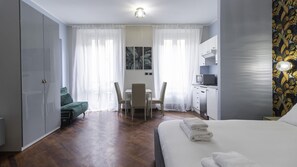 A hotel room with a bed, a desk with chairs, a kitchenette, and a wardrobe. - Italianway Easy - Venezia 33 - A (Milan)
