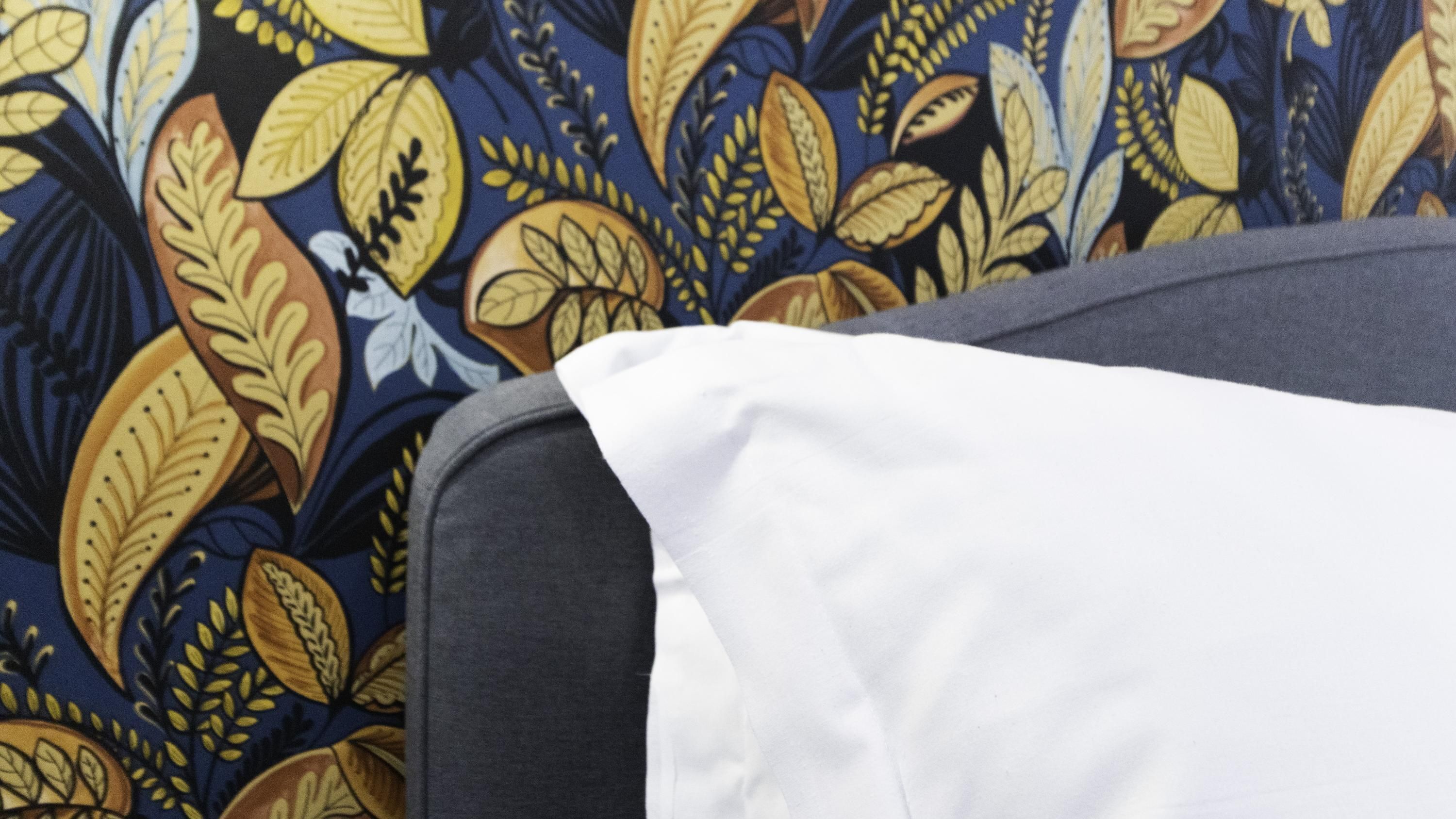 Un gros plan d’un coussin blanc posé sur un canapé gris, le tout sur un fond à motifs.