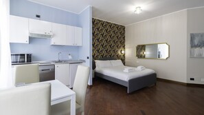 A modern hotel room with a kitchenette, a bed with neatly made white linens, a large mirror, and a wooden floor. - Italianway Easy - Venezia 33 - A (Milan)