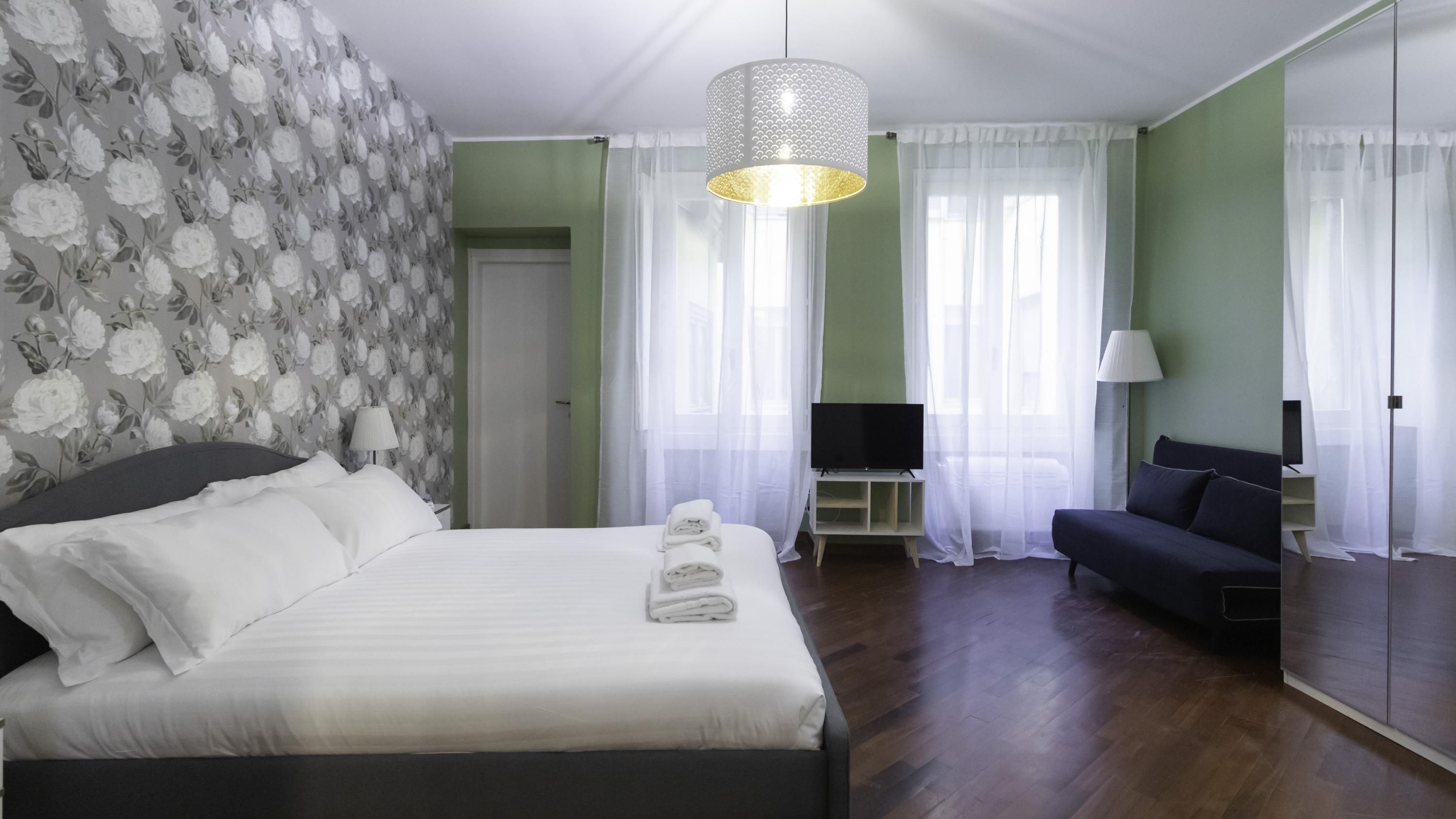 A hotel room with a bed, a sofa, a TV, and a mirror.