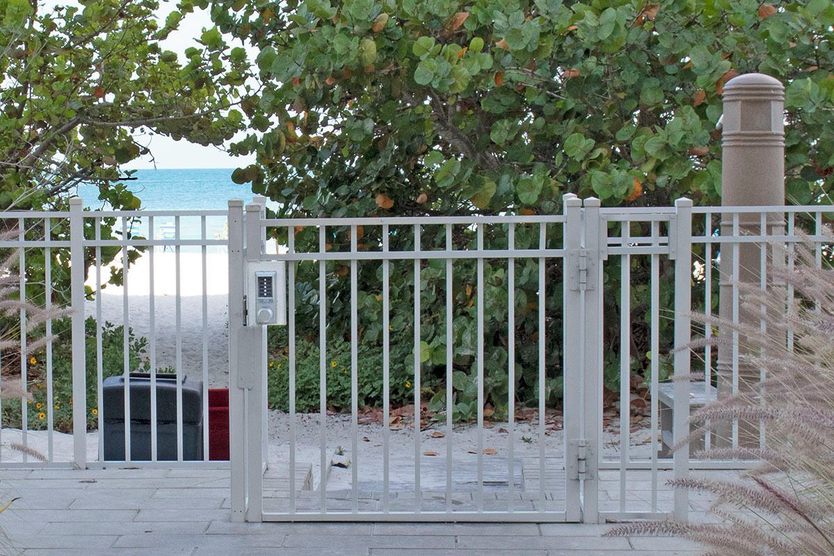 A gated entrance with a metal gate, a trash bin, and a tree with green leaves.