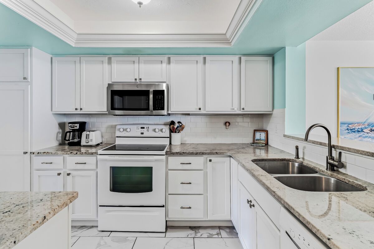 A modern kitchen with white cabinetry, a stainless steel sink, a microwave, a stove, and a coffee maker.