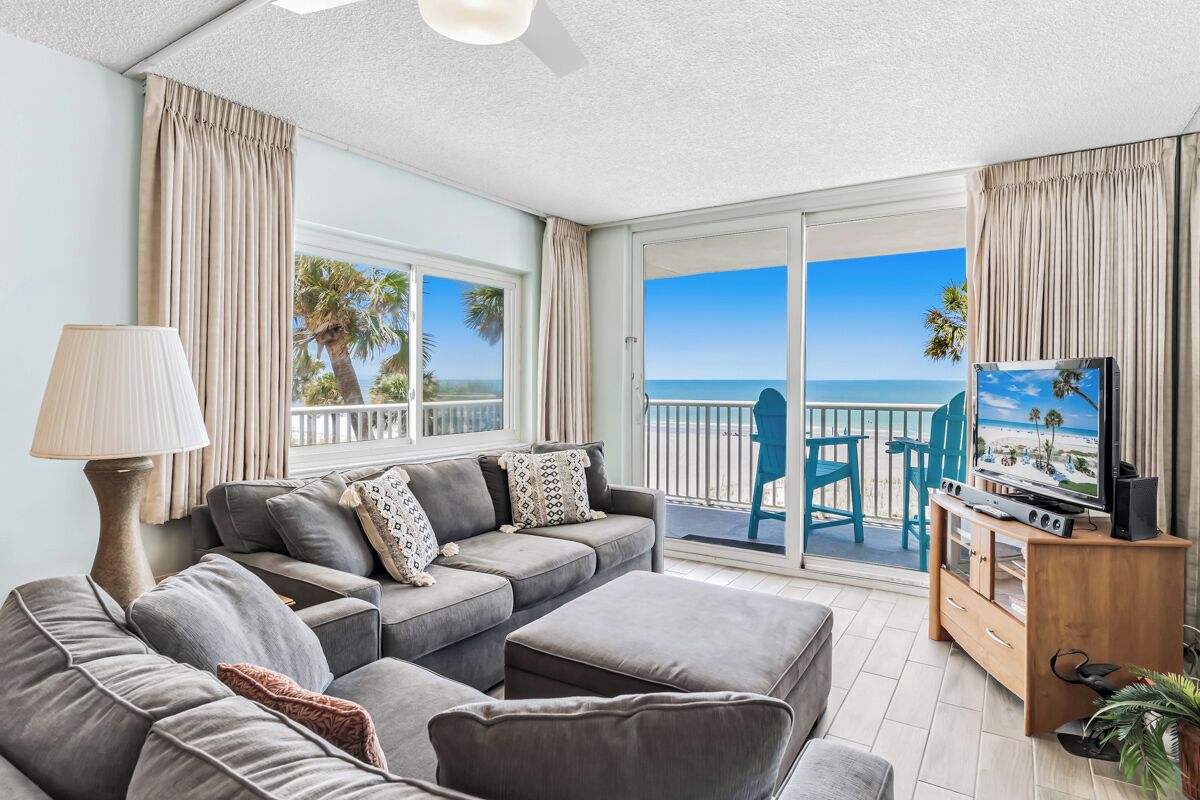 Una sala de estar con sofá, mueble para televisor y vista a la playa.
