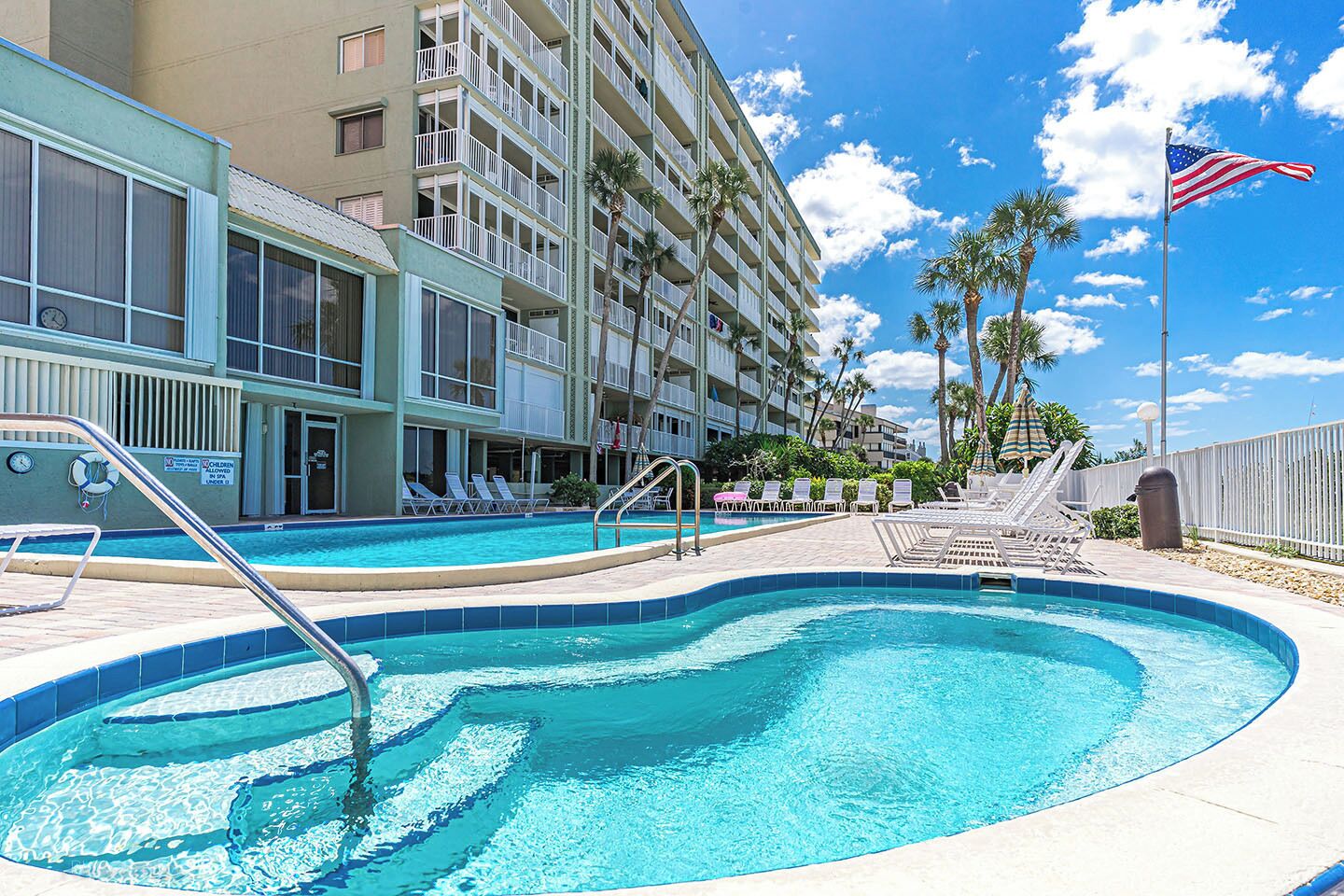 Un hôtel doté d’une piscine, de chaises longues et de palmiers.