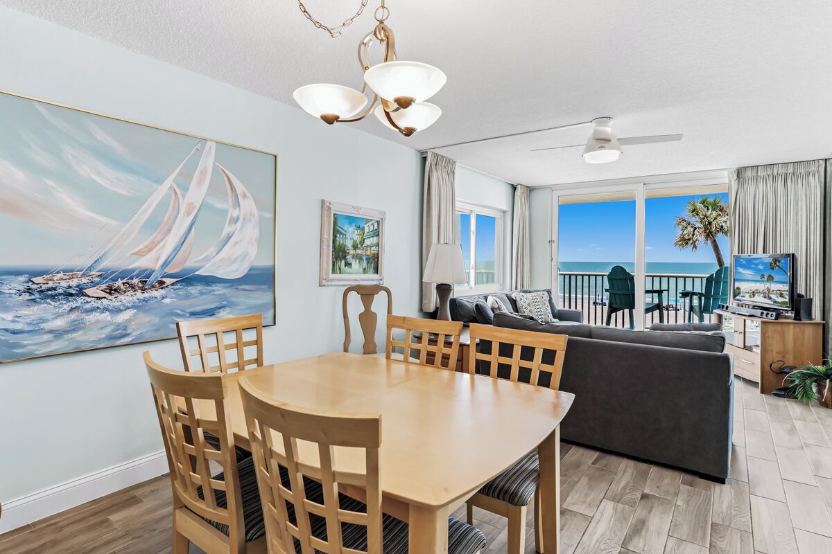 A living room with a dining area, a sofa, a TV, and a view of the ocean.