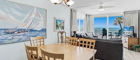 A living room with a dining area, a sofa, a TV, and a view of the ocean.