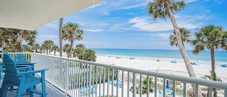 A balcony with a view of a beach, palm trees, and a clear sky.