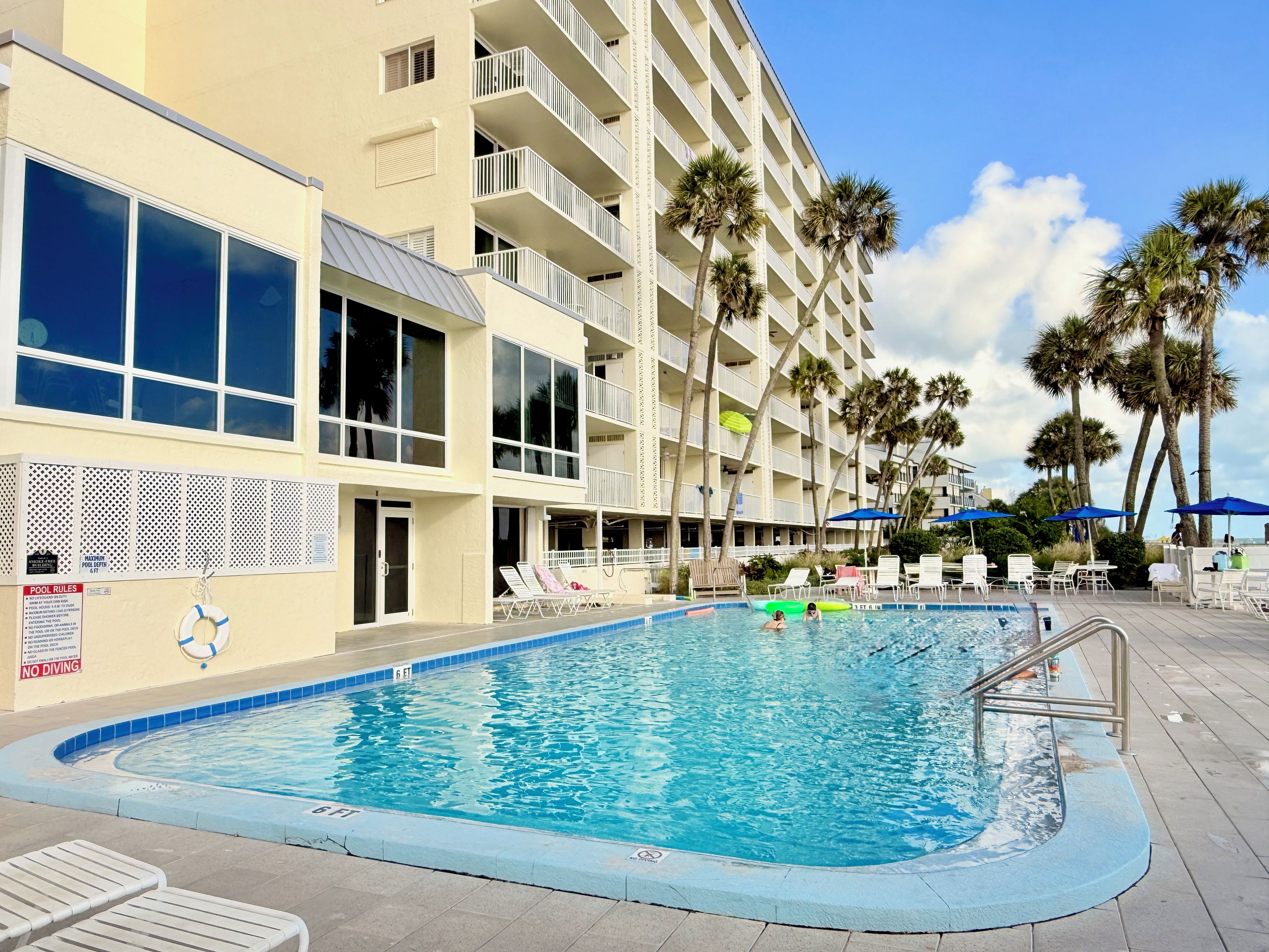 Un espace piscine d’hôtel avec une piscine à l’eau cristalline, des chaises longues et des palmiers.