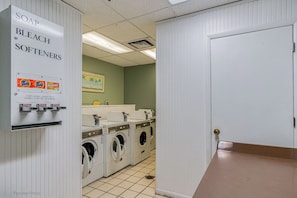 A laundry room with a coin-operated washer and dryer, soap, bleach, and softeners dispenser, and a door to the right. - GULF FRONT CORNER UNIT Condo! Sand Castle I 301 (Indian Shores)