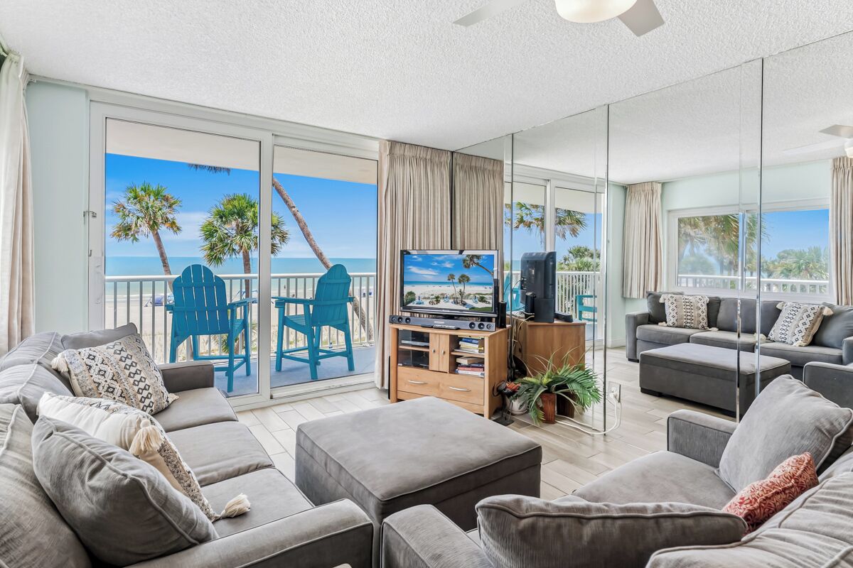 A modern living room with a large sliding glass door leading to a balcony with a view of palm trees and the sea.