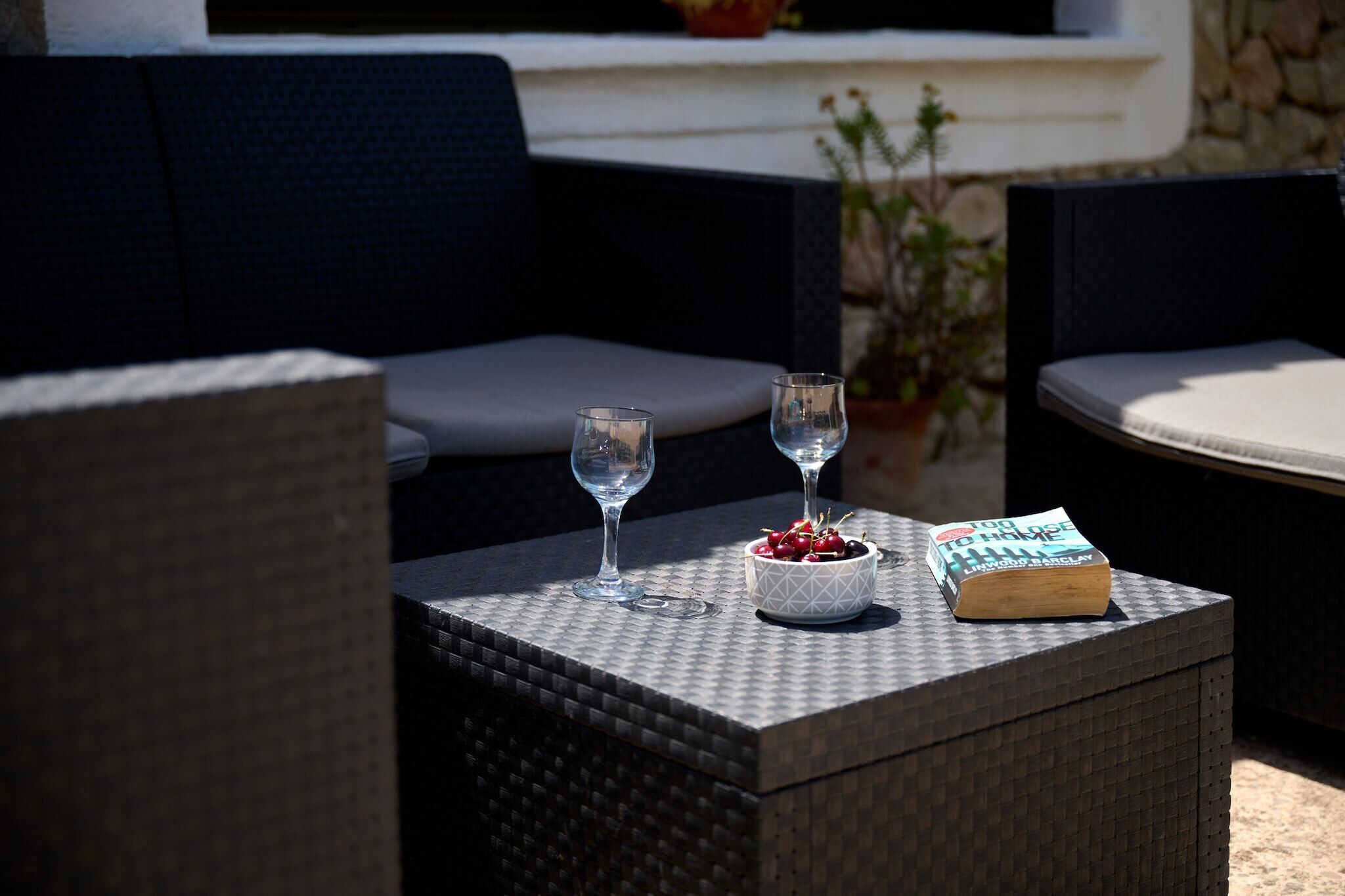 A wicker table with two glasses, a bowl of cherries, and a book.