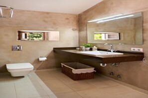 Een moderne badkamer met een wit toilet, een grote spiegel, een wastafel met donker aanrechtblad en een rieten mandje.
