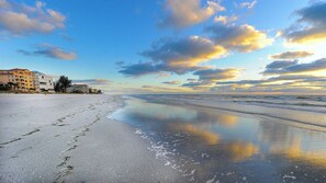 Ein Strand mit blauem Himmel, ruhiger See und Gebäuden im Hintergrund.