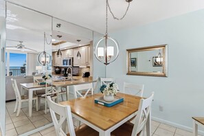 A dining area with a wooden table and white chairs, a vase with flowers, and a mirror on the wall. - Gulf Front Getaway! Sand Castle I 307 (Indian Shores)