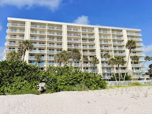 A multi-story hotel with balconies, palm trees, and a sandy foreground. - Gulf Front Getaway! Sand Castle I 307 (Indian Shores)