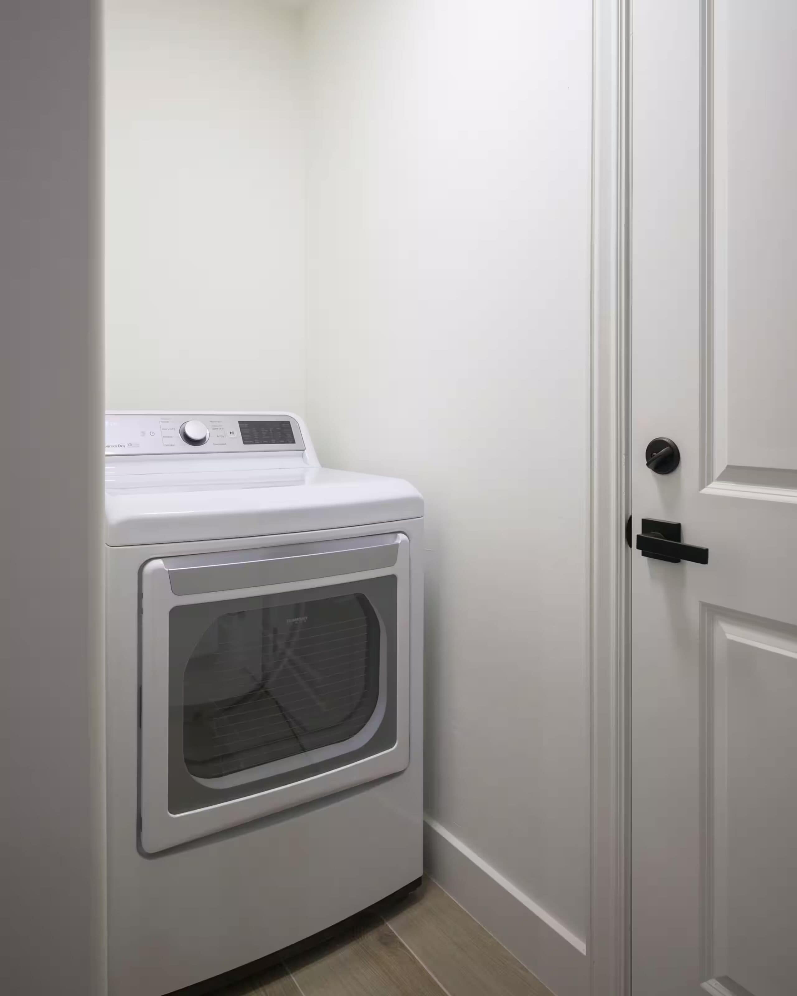 A compact, white, front-loading washer and dryer unit in a small laundry room with a door to the right.