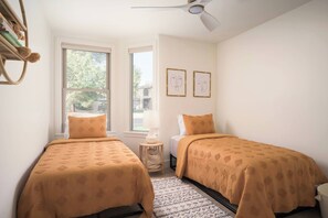 Ein Schlafzimmer mit zwei Betten, einem Fenster, einem Deckenventilator und zwei gerahmten Kunstwerken an der Wand.