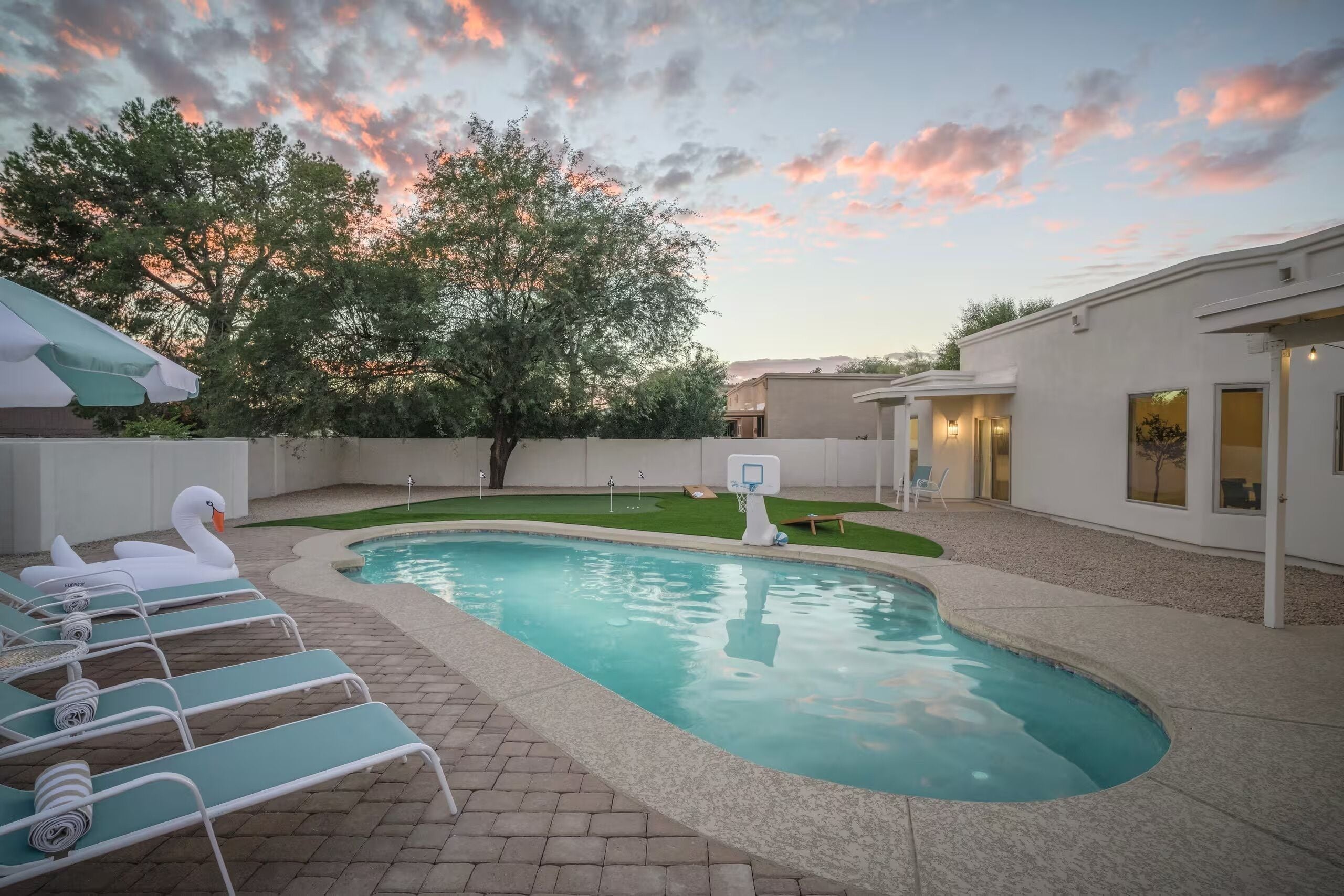 A swimming pool with lounge chairs and a basketball hoop in a backyard.