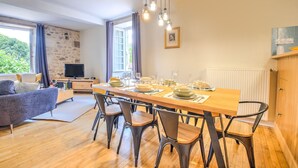 Zona pranzo con tavolo in legno apparecchiato per quattro persone, divano e TV sullo sfondo.