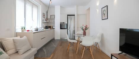 A modern kitchen with a dining area, a sofa, and a TV.
