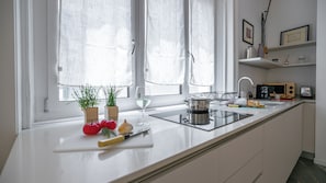 Eine moderne Küche mit weißer Arbeitsplatte, Spüle, Herd und einem Fenster mit durchsichtigen Vorhängen.