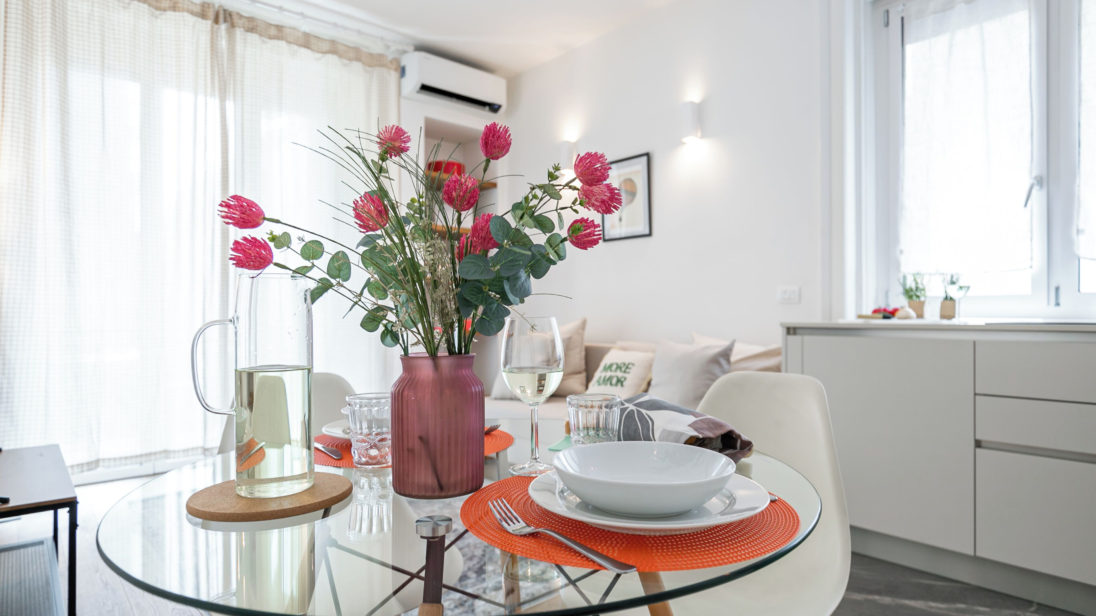 A dining area with a glass table, a vase with flowers, and a white plate.