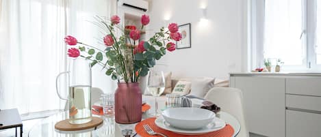 A dining area with a glass table, a vase with flowers, and a white plate.