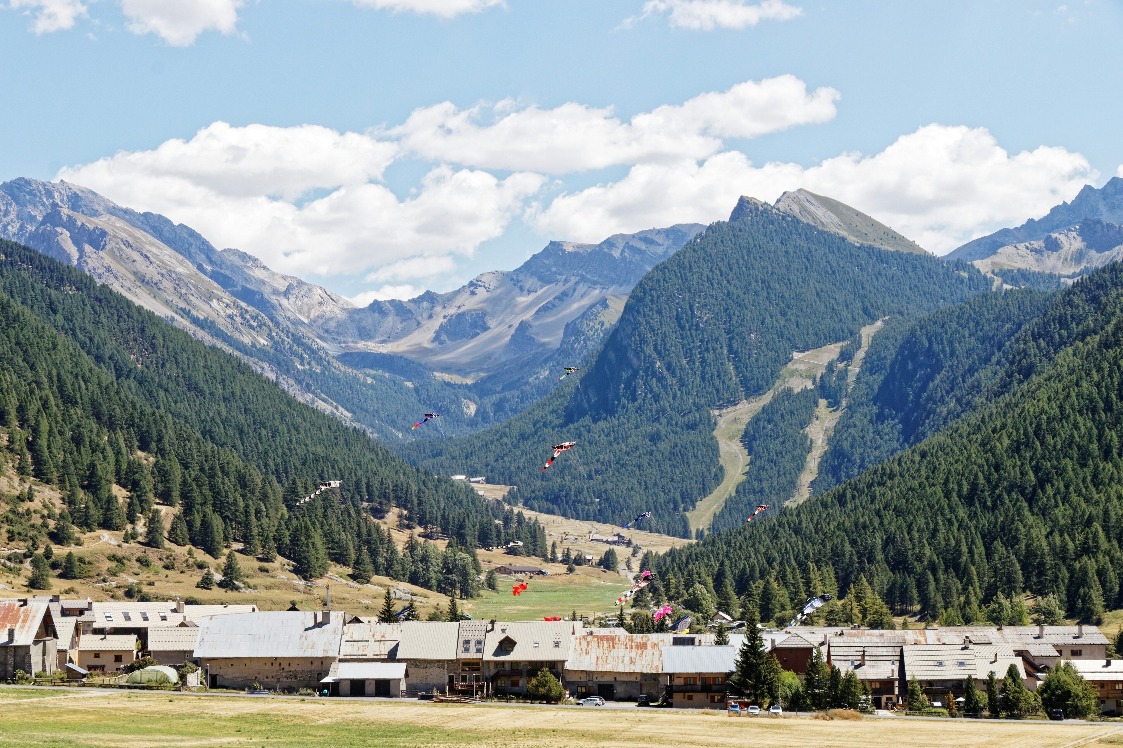 Ein Bergdorf mit traditionellen Häusern, einer Skipiste und blauem Himmel.