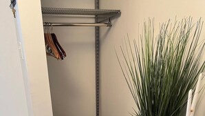 Una habitación compacta con un escritorio de madera, una planta en maceta, una estantería metálica y un perchero.