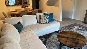 Una sala de estar moderna con un sofá modular, una mesa de centro redonda y un comedor con mesa y sillas.