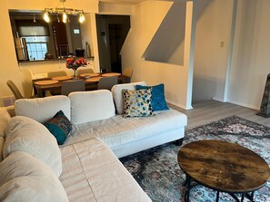 Ein modernes Wohnzimmer mit einem Ecksofa, einem runden Couchtisch und einem Essbereich mit Tisch und Stühlen.