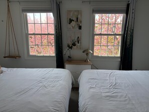 Une chambre avec deux lits, un bureau avec une lampe et des fenêtres donnant sur des cerisiers en fleurs, aux pétales roses.