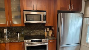 Una cocina con armarios de madera, un microondas de acero inoxidable, un refrigerador y una estufa a gas.