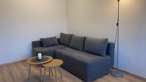 Ein modernes Wohnzimmer mit einem grauen Sofa, einem kleinen runden Tisch und einer Stehlampe.