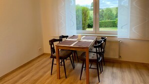 Ein Essbereich mit Tisch und Stühlen, einem Fenster mit Jalousien und einer Heizung.