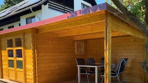 Eine Holzlaube mit überdachter Terrasse, einem Esstisch und Stühlen.