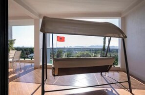 Un balcó amb una cadira bressol, una bandera i vista a la ciutat.